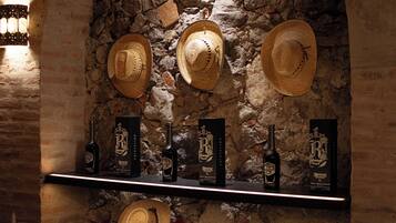 Un estante con sombreros y botellas frente a una pared de piedra.