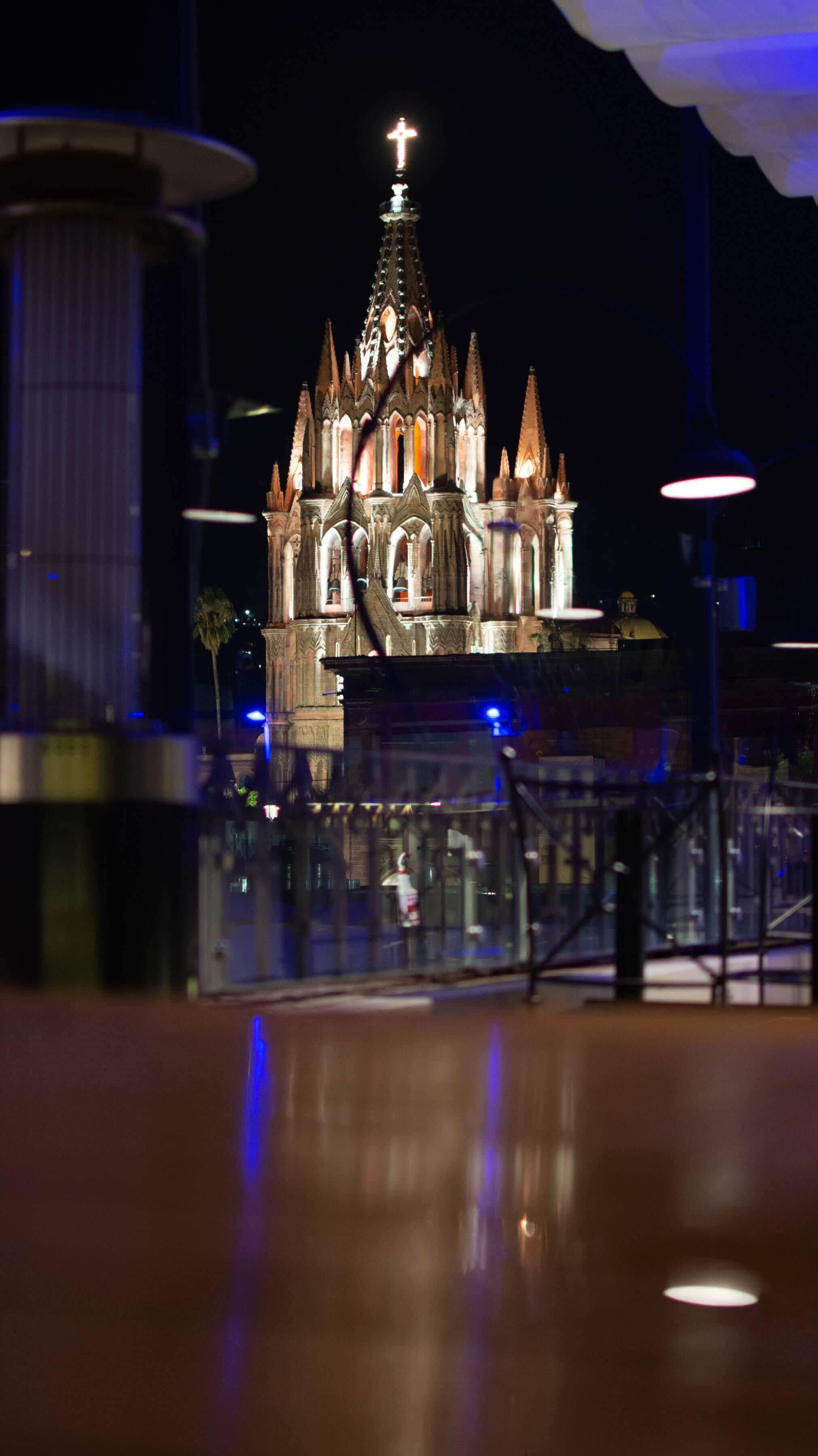 Une cathédrale dotée d’une flèche imposante et surmontée d’une croix, illuminée la nuit.