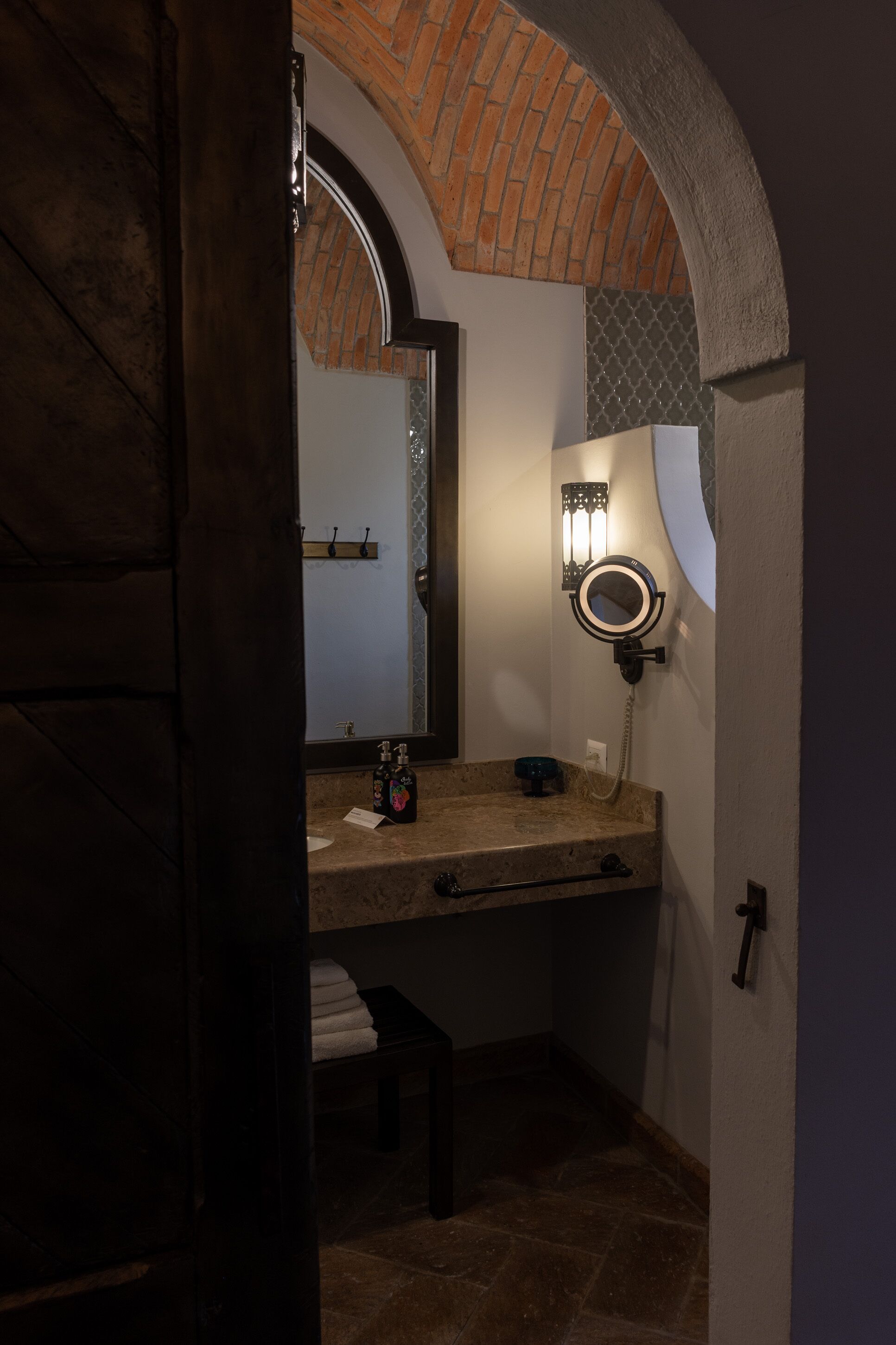 A bathroom with a stone countertop, a mirror with lights, and a towel rack.