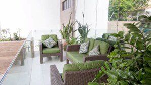 A modern outdoor seating area with wicker furniture and green cushions, surrounded by potted plants. - San Phillip Flat Hotel (Fortaleza)