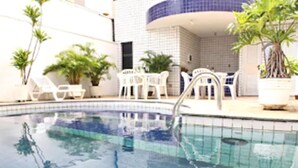 A swimming pool with a tiled deck, surrounded by potted plants and white outdoor furniture. - San Phillip Flat Hotel (Fortaleza)