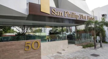 Exterior do Hotel San Phillip Flat, com um destaque para o sinal '50', arquitetura moderna e entrada de vidro.