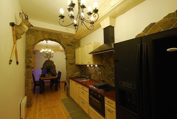 Una cocina con paredes de piedra, armarios de madera, un refrigerador negro y una araña.