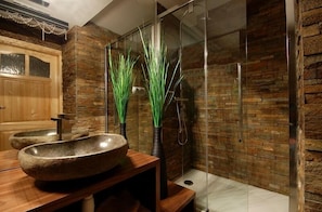 A modern bathroom with a stone sink, wooden vanity, and a glass shower enclosure.
