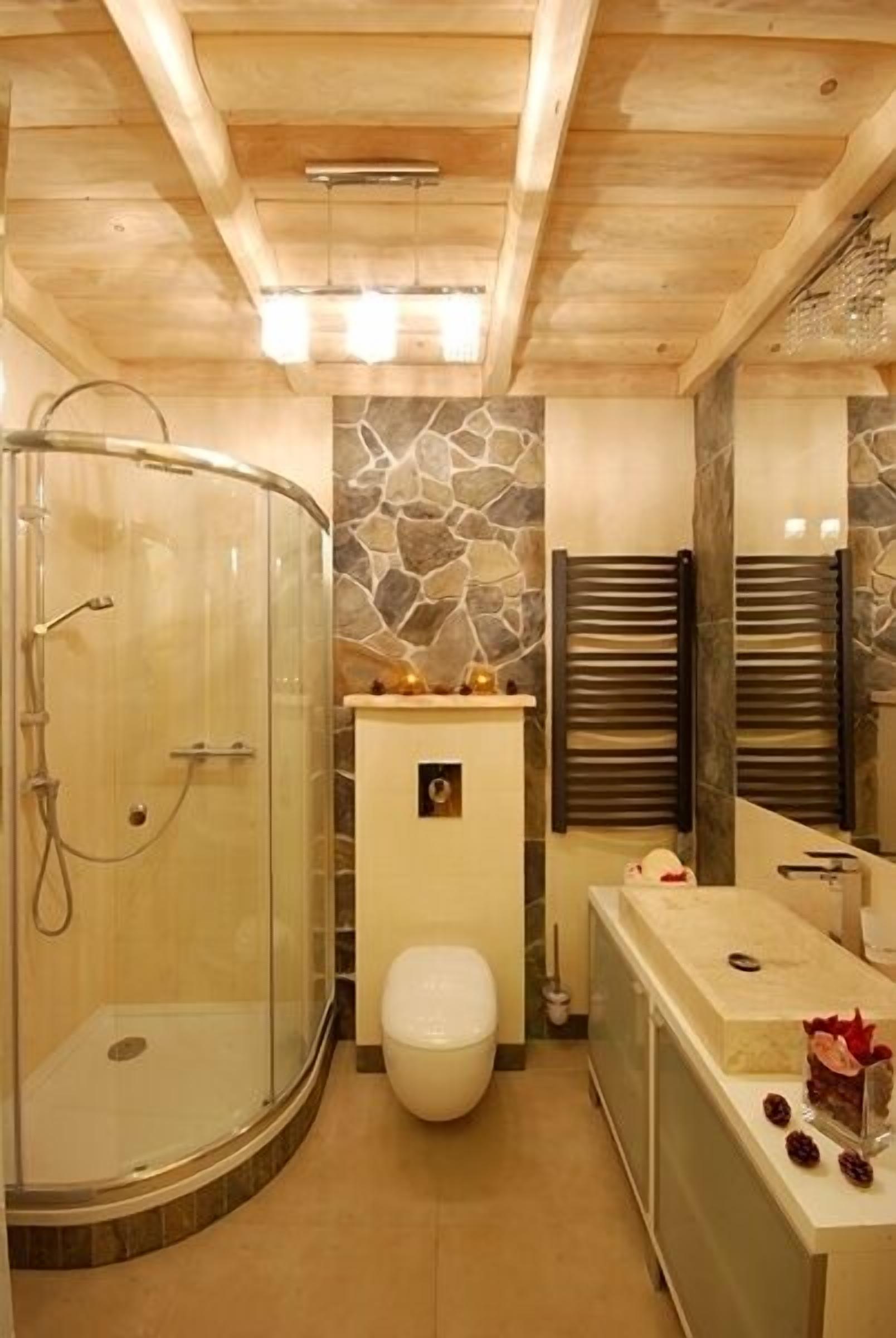 Un baño moderno con cabina de ducha de vidrio, un muro decorativo de piedra y techo de madera.