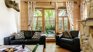 A cozy living room with a wooden interior, two leather sofas with patterned cushions, a coffee table with pastries, and a stone fireplace.