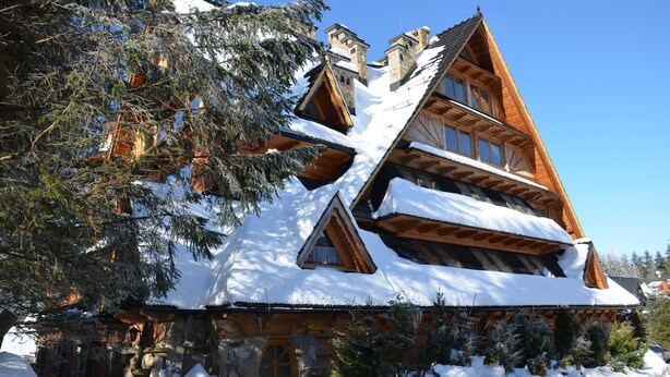 A log cabin with a steeply pitched roof, stone foundation, and wooden exterior.