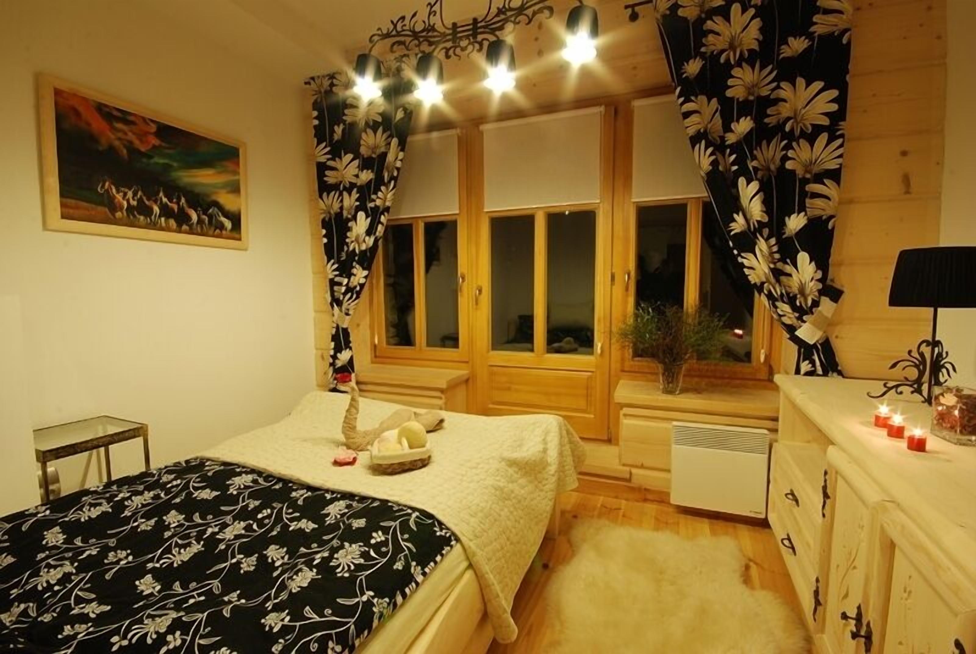 A bedroom with a bed, a window with curtains, a painting on the wall, and a bedside table with a lamp.