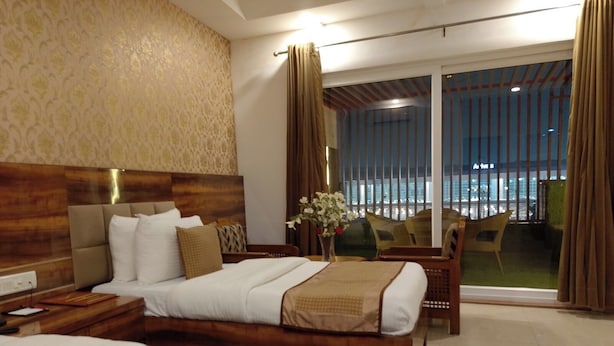 Een hotelkamer met twee bedden, een houten hoofdbord, een nachtkastje, een bureau en uitzicht op de stad door grote ramen.