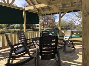 A wooden deck with outdoor seating, including chairs and a table, overlooking a body of water and trees.
