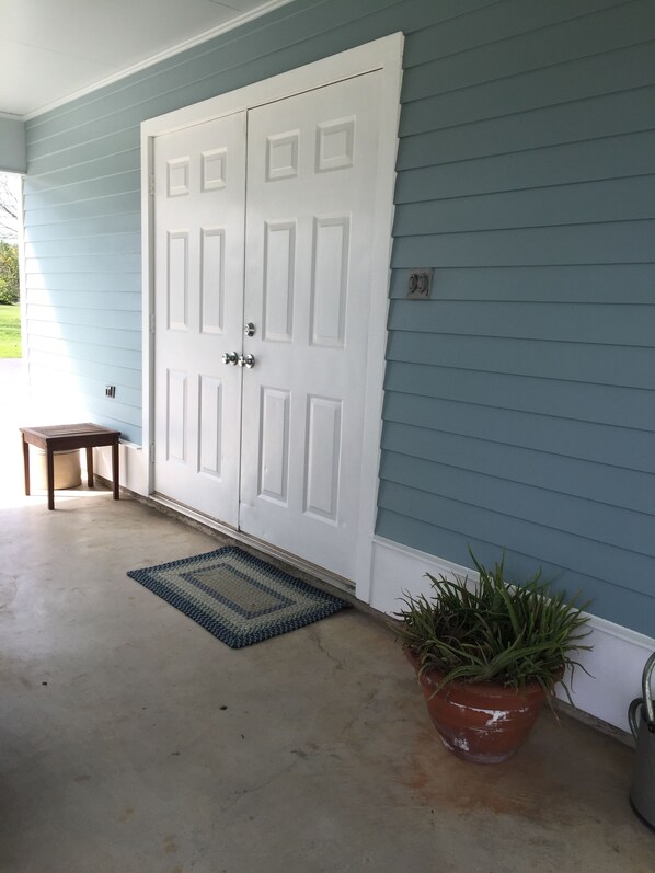 A front door with a doormat, a small wooden bench, and a potted plant.