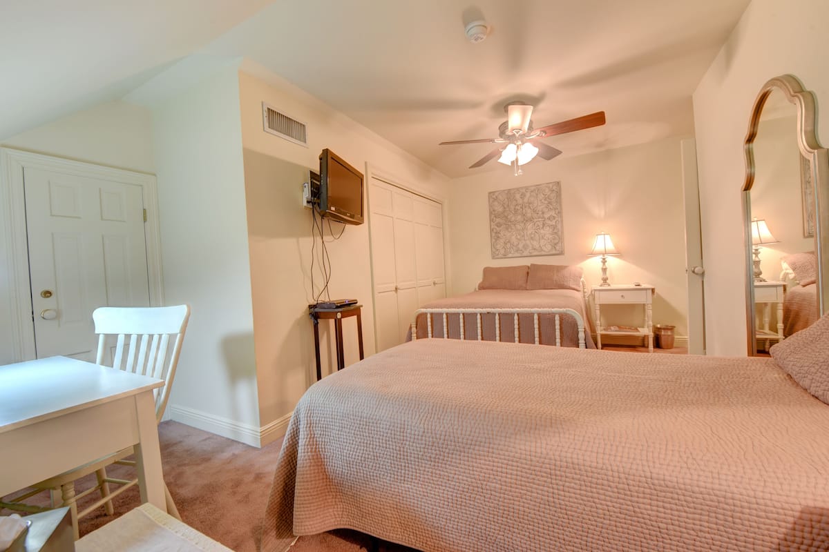 A bedroom with a bed, a desk, a chair, a ceiling fan, and a television.