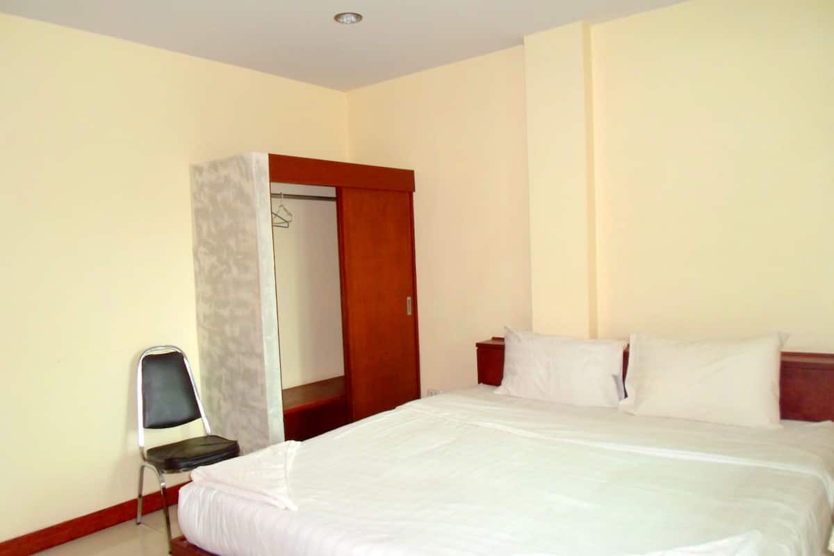 A hotel room with a bed, a chair, a wardrobe, and a nightstand.