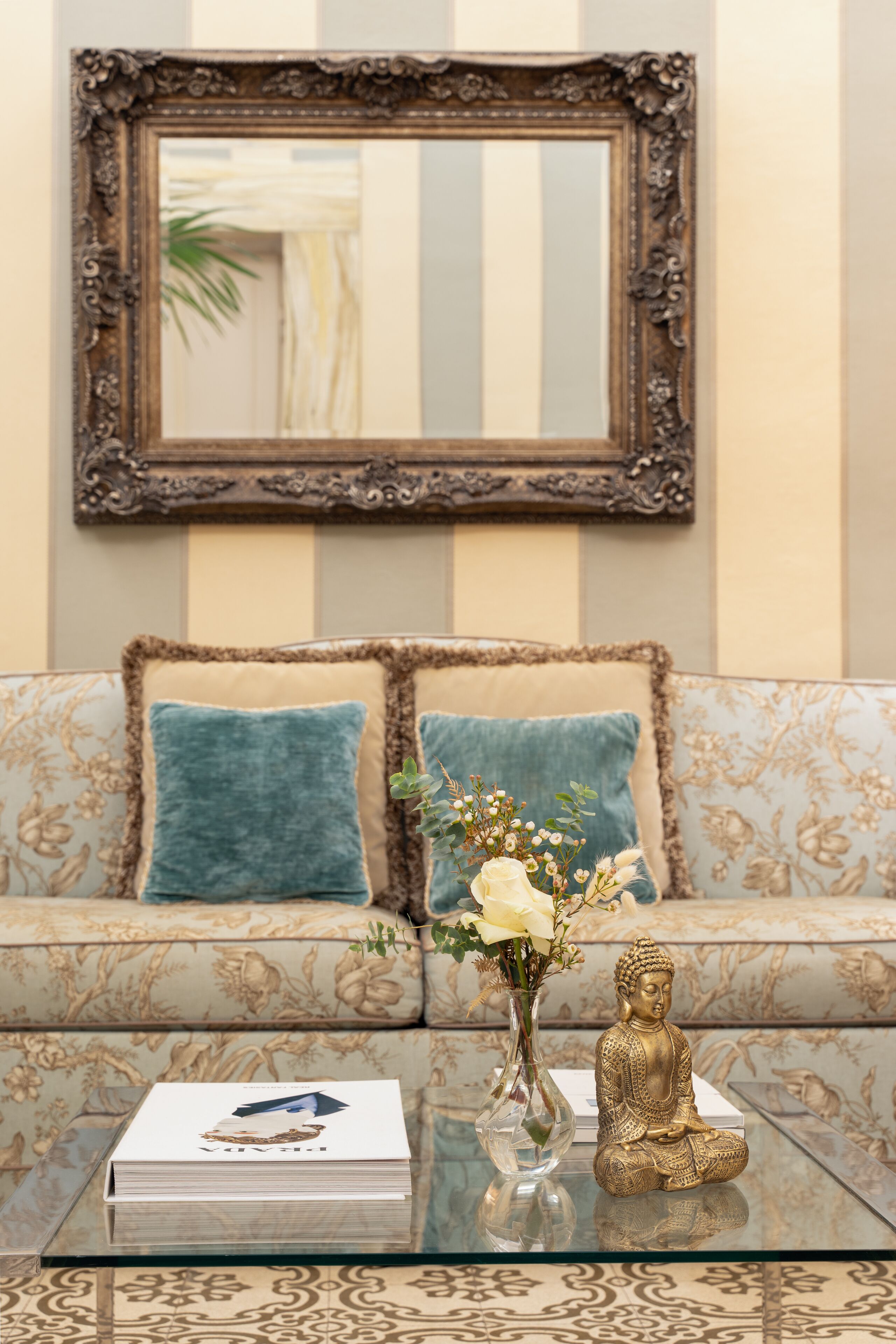 A living room with a sofa, a glass coffee table, a Buddha statue, and a framed mirror on the wall.
