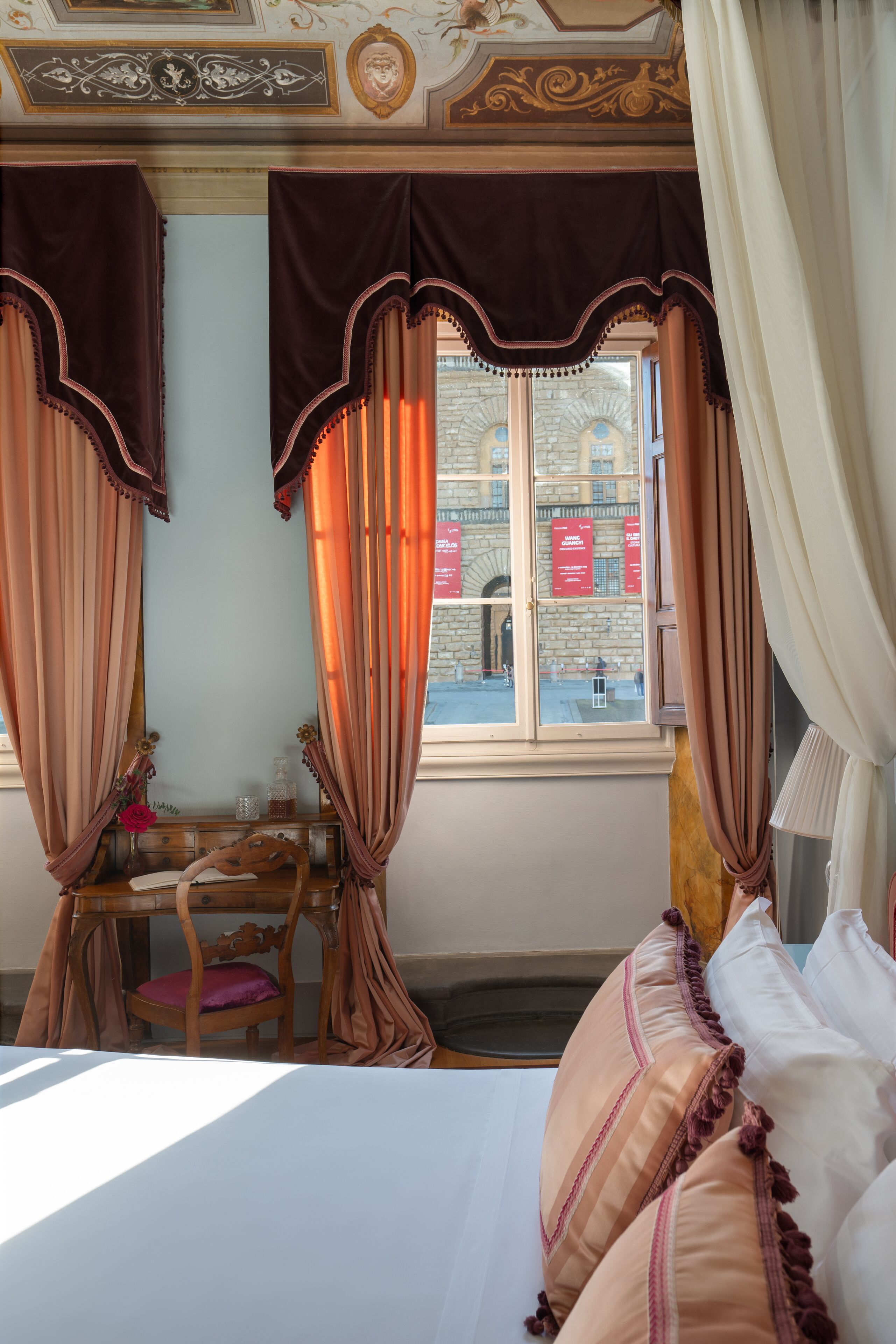 A room with a bed, a wooden chair, a small table with a vase, and curtains.