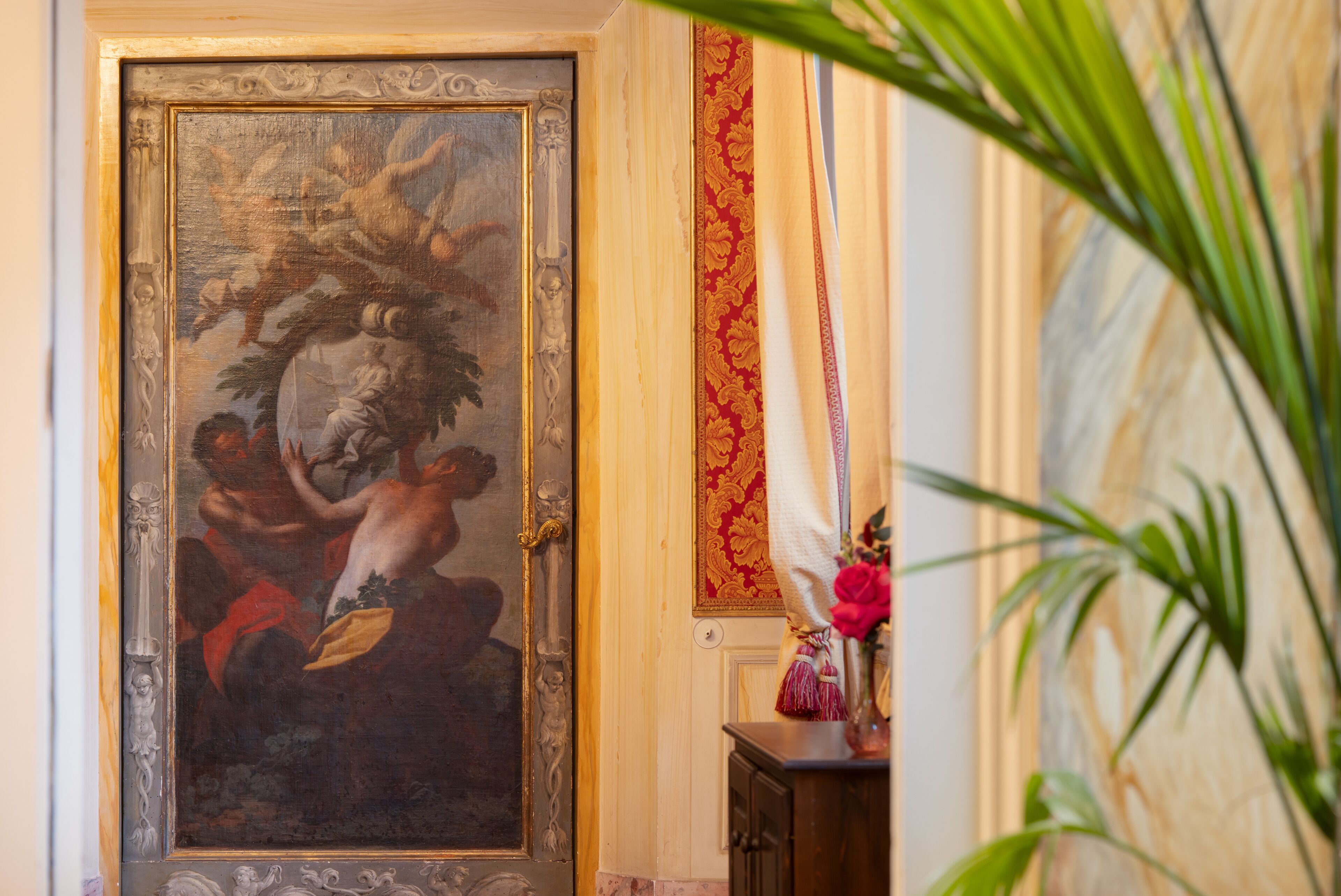 A classical painting on a wall, a wooden cabinet, and a red patterned curtain.