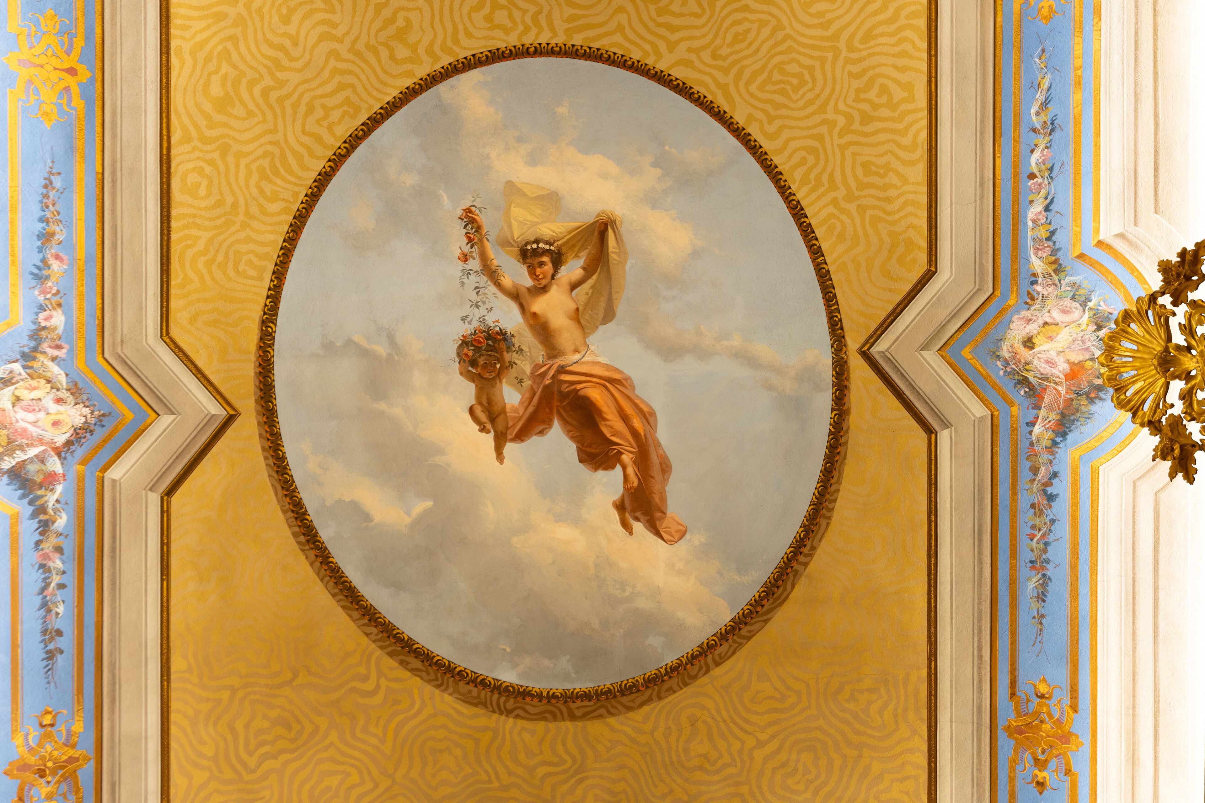 A ceiling with a circular fresco of a mythological scene, ornate gold and blue patterns, and floral decorations.