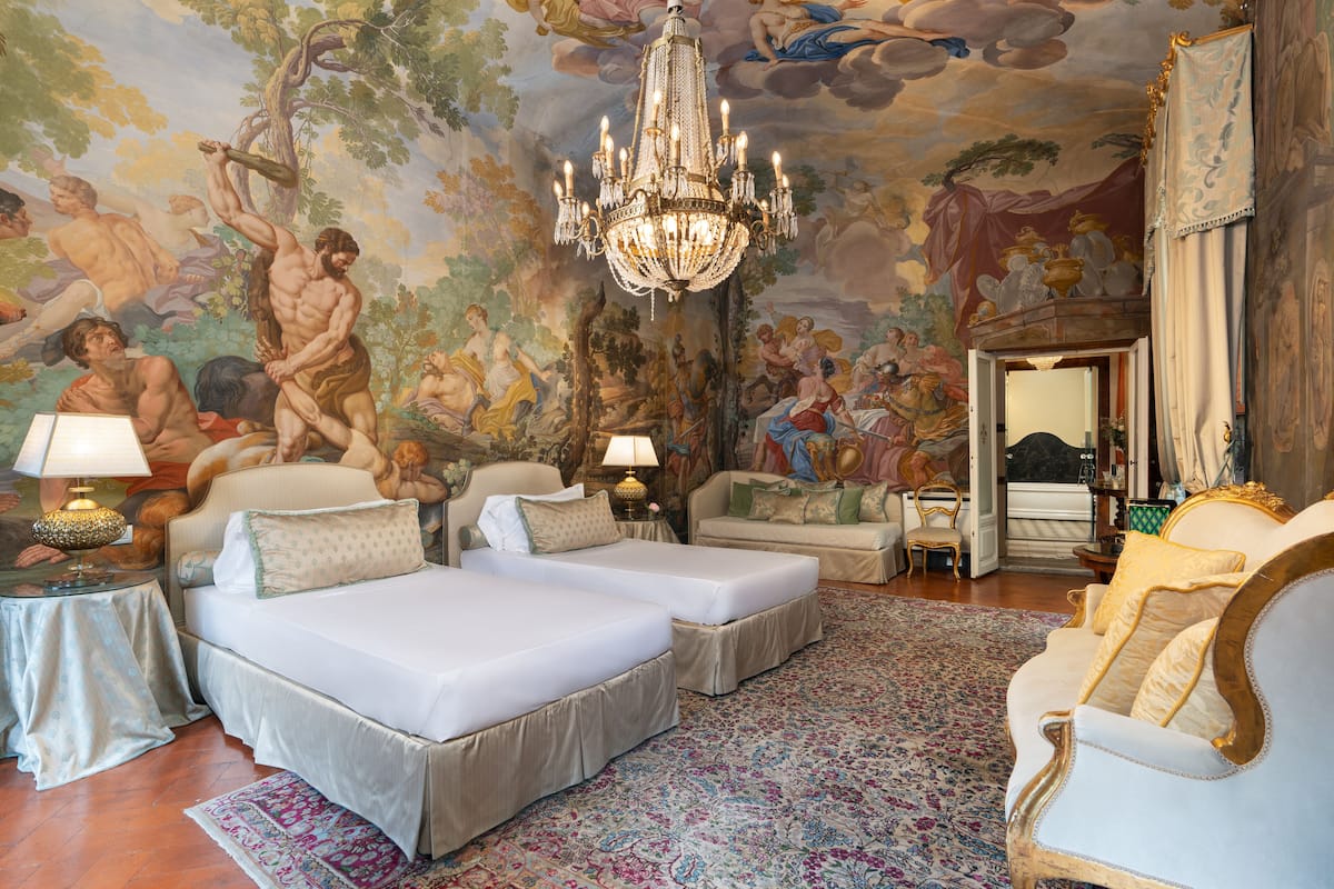 Un dormitorio lujoso con dos camas, una araña, un mural y muebles clásicos.