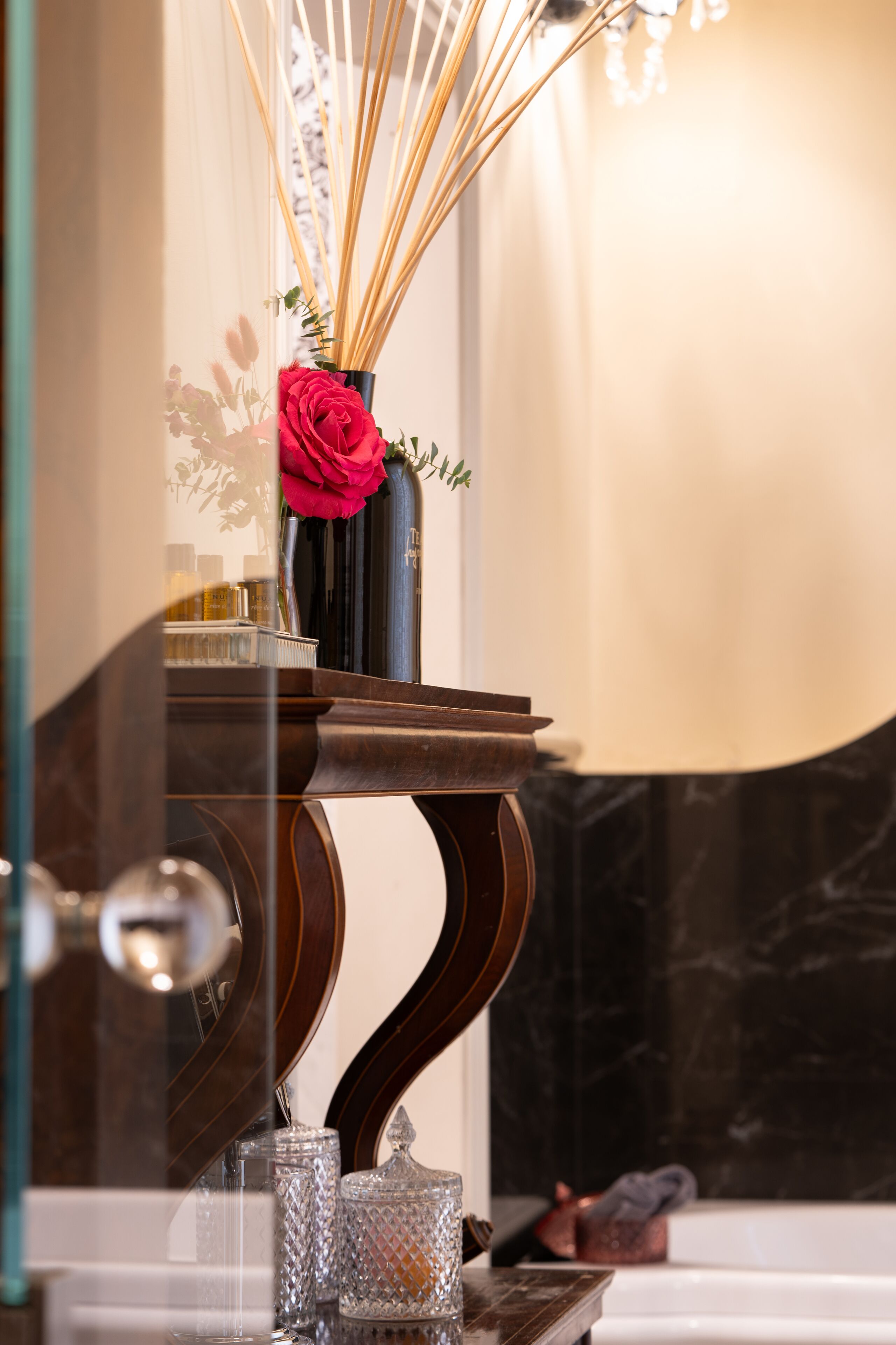 A bathroom vanity with a vase of red roses, a mirror, and a marble countertop.