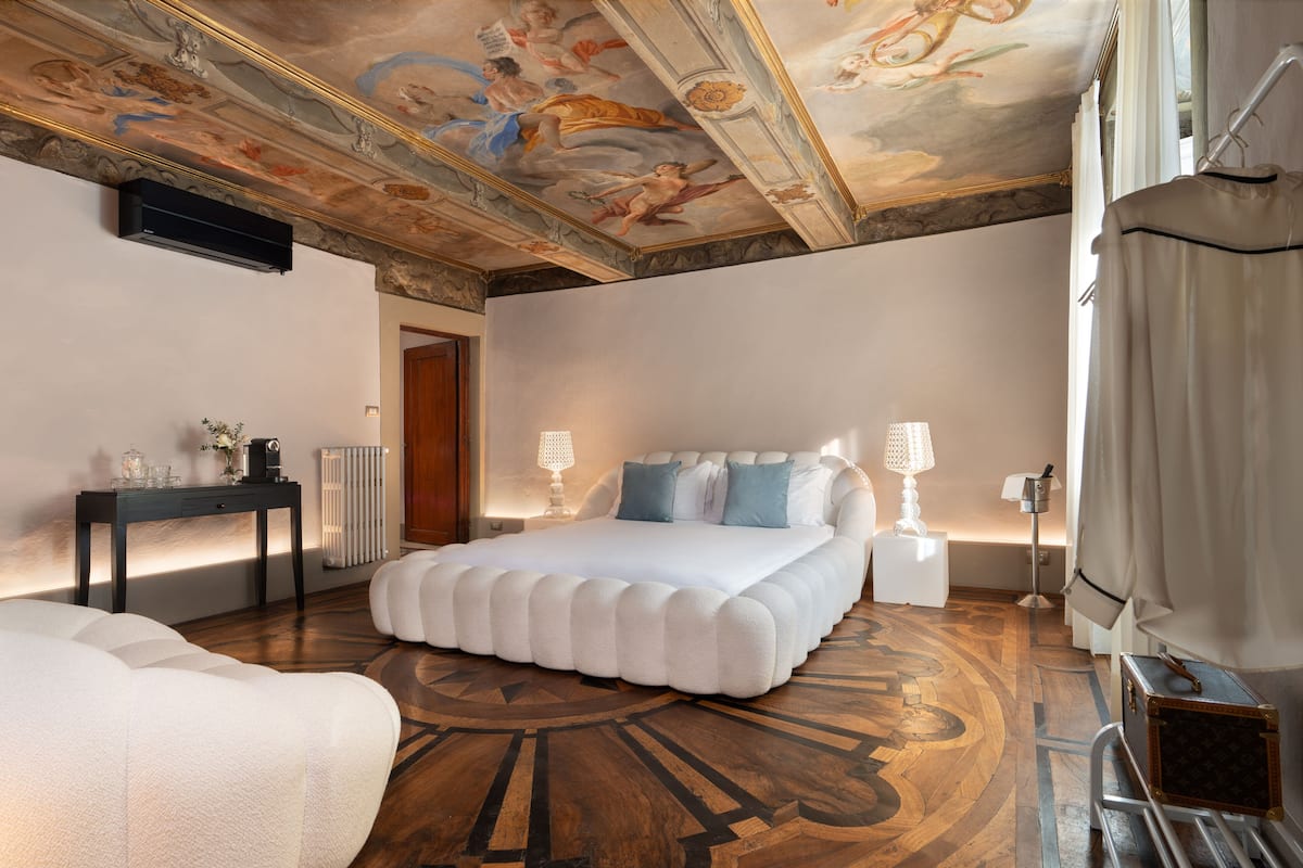 Un dormitorio amplio con una cama grande, una mesita de noche, una lámpara y un techo con un fresco detallado.
