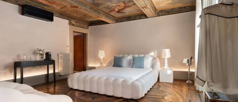 A spacious bedroom with a large bed, a bedside table, a lamp, and a ceiling with a detailed fresco.