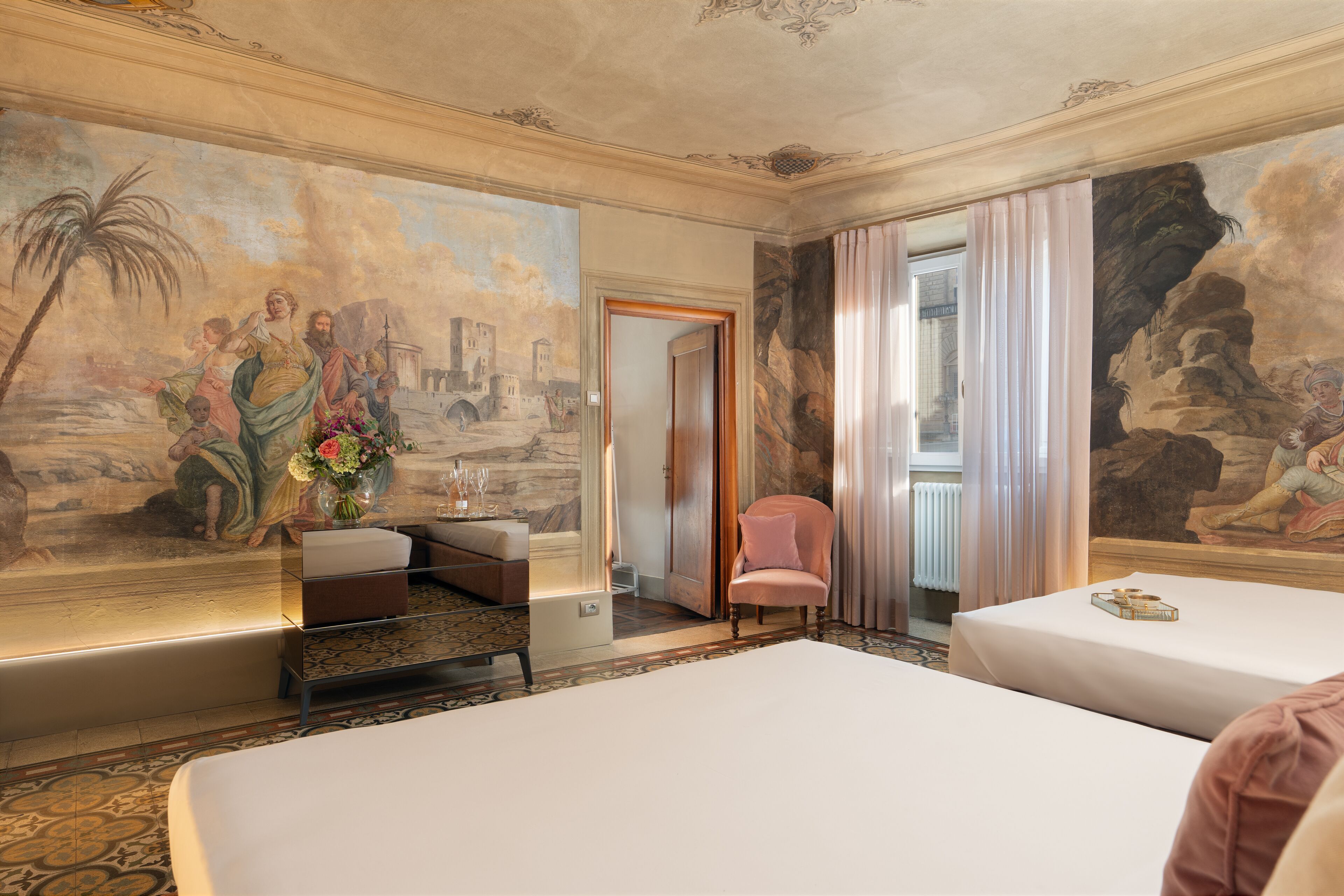 Una habitación de hotel con dos camas, una silla, una mesita y un cuadro en la pared.