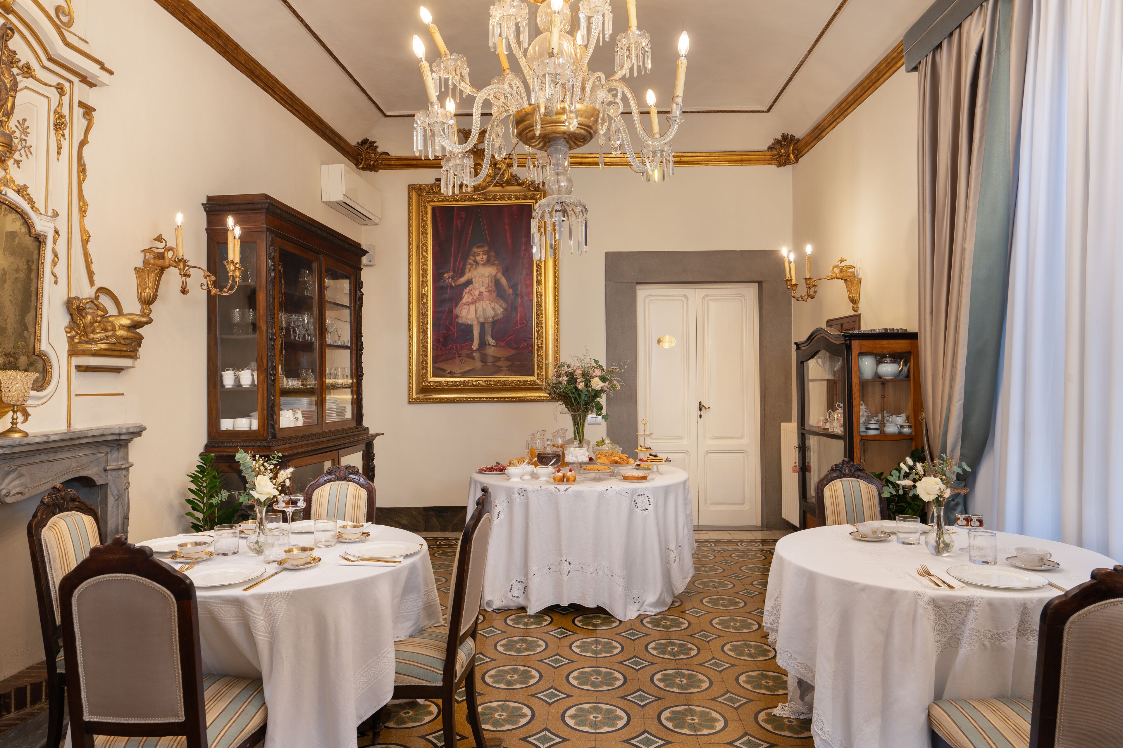 Une salle à manger élégante, ornée de lustres, d’un grand tableau et d’une cheminée.