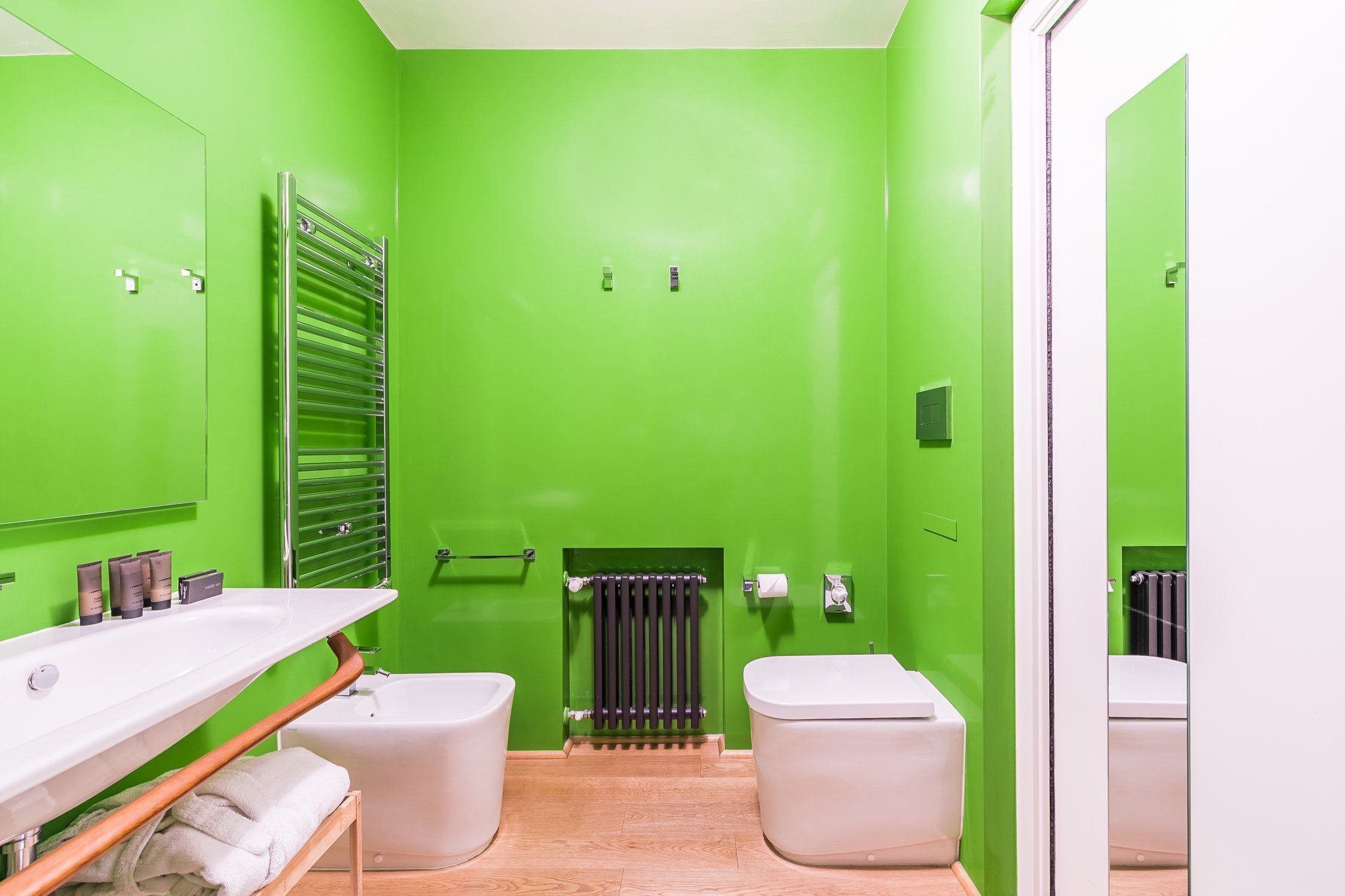 A bathroom with a green wall, a white sink, two toilets, and a towel rack.