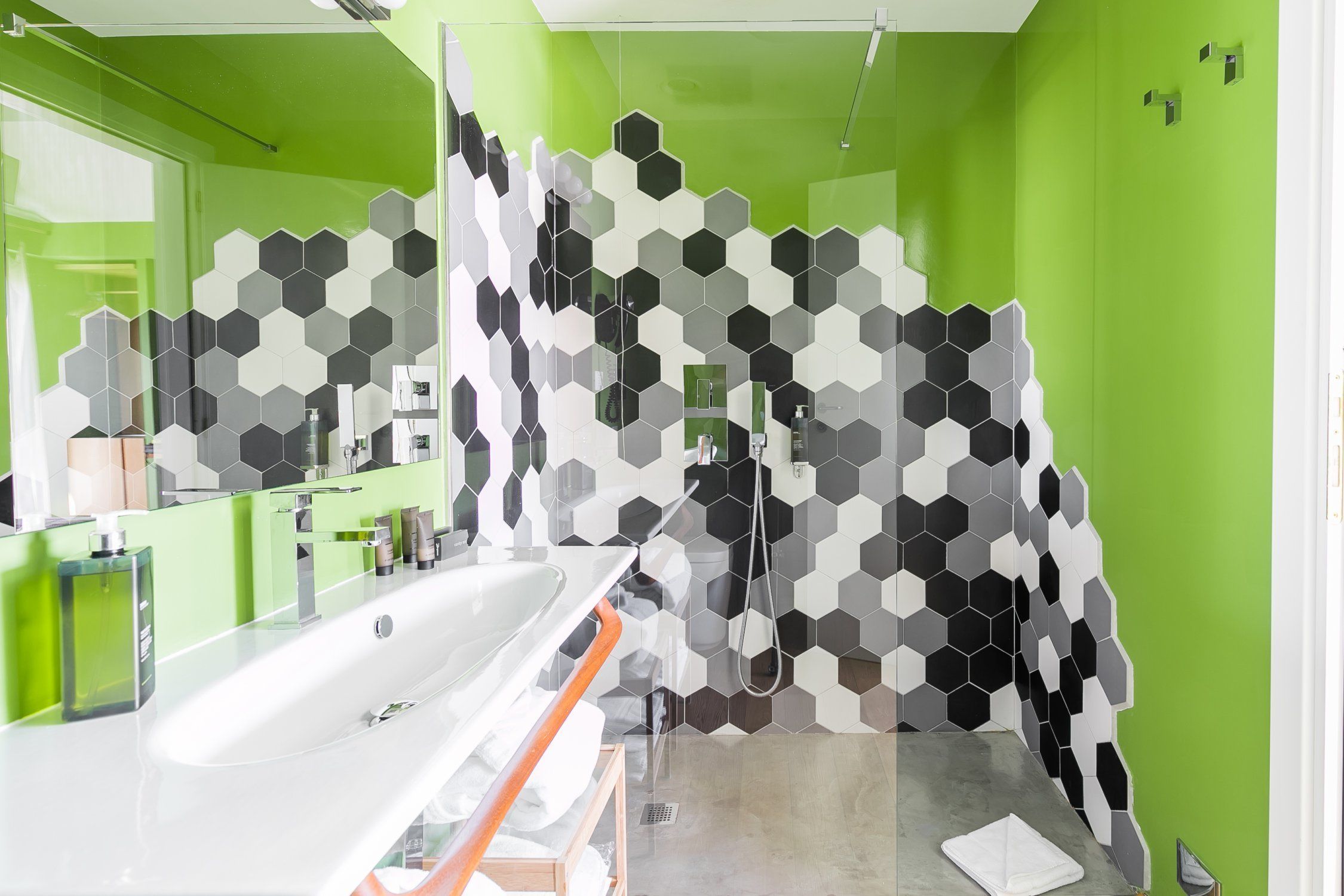A modern bathroom with a green wall, a white sink, and a shower area.
