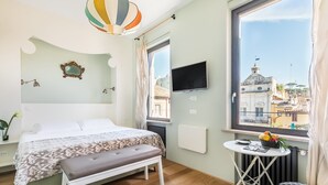 Ein Schlafzimmer mit Bett, Bank, Tisch und einem Fenster mit Blick auf die Stadt.