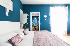 A bedroom with a large bed, a nightstand, a mirror, and a bathroom visible through an open door. - Rarity Suites (Rome)