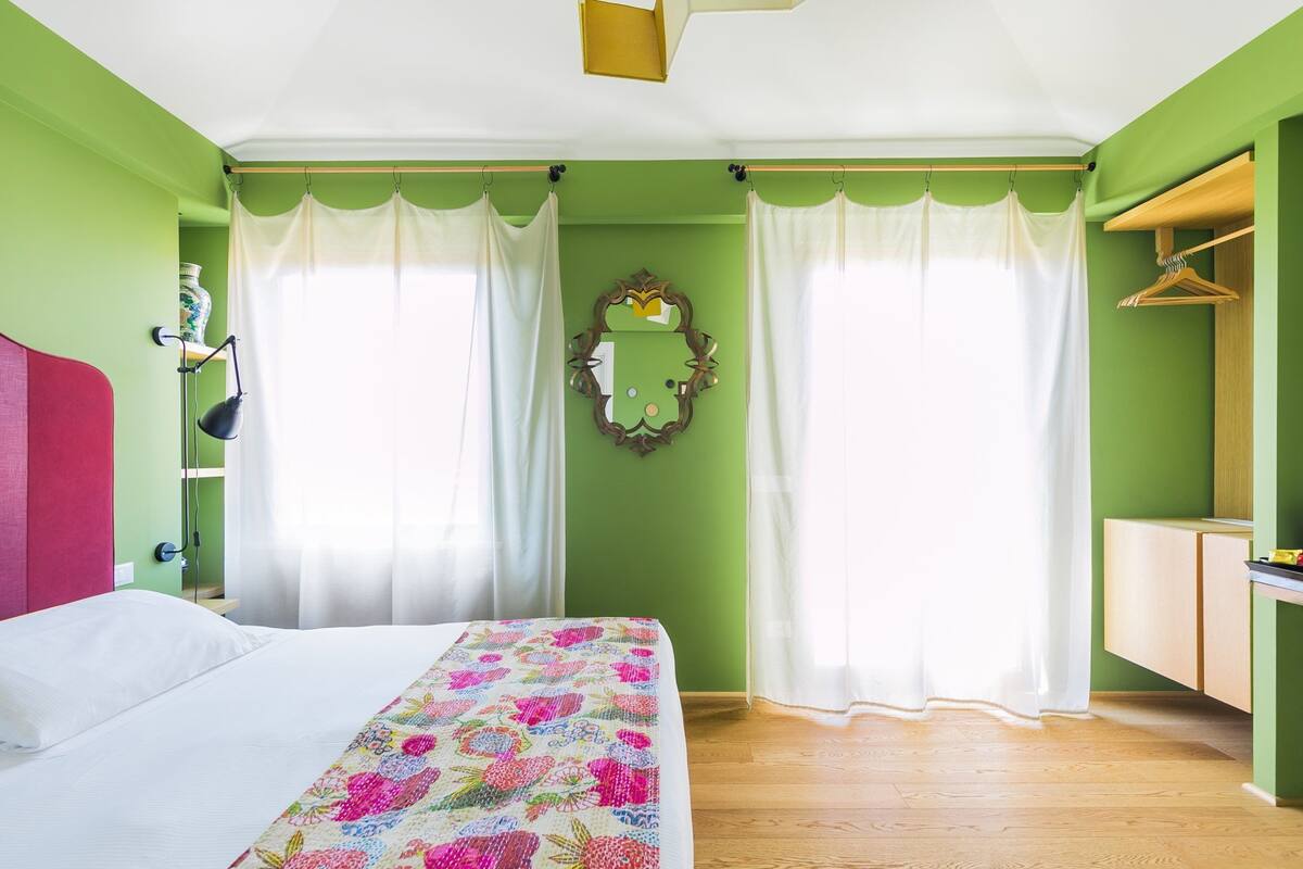 A bedroom with a bed, a mirror, a wardrobe, and a window with curtains.