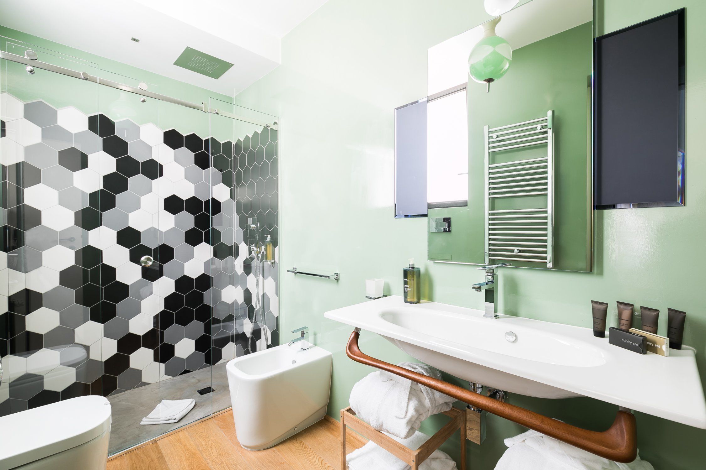 A modern bathroom with a glass shower enclosure, a white bathtub, a large sink with a vanity, and a towel rack.