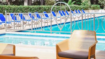 Un área de piscina con sillones de descanso azul y blanco, una escalera metálica para la piscina y una silla de mimbre al frente.