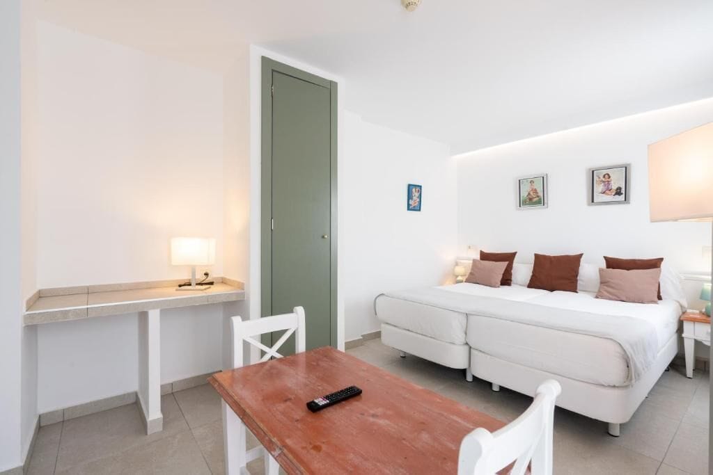 A small, clean room with a bed, a desk, and a chair. There are wall-mounted pictures and a lamp on the desk.