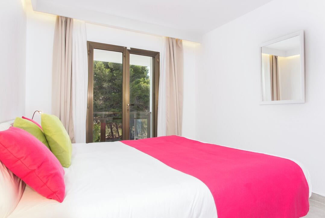 Een slaapkamer met een groot bed, een balkon met glazen deuren en uitzicht op groen.