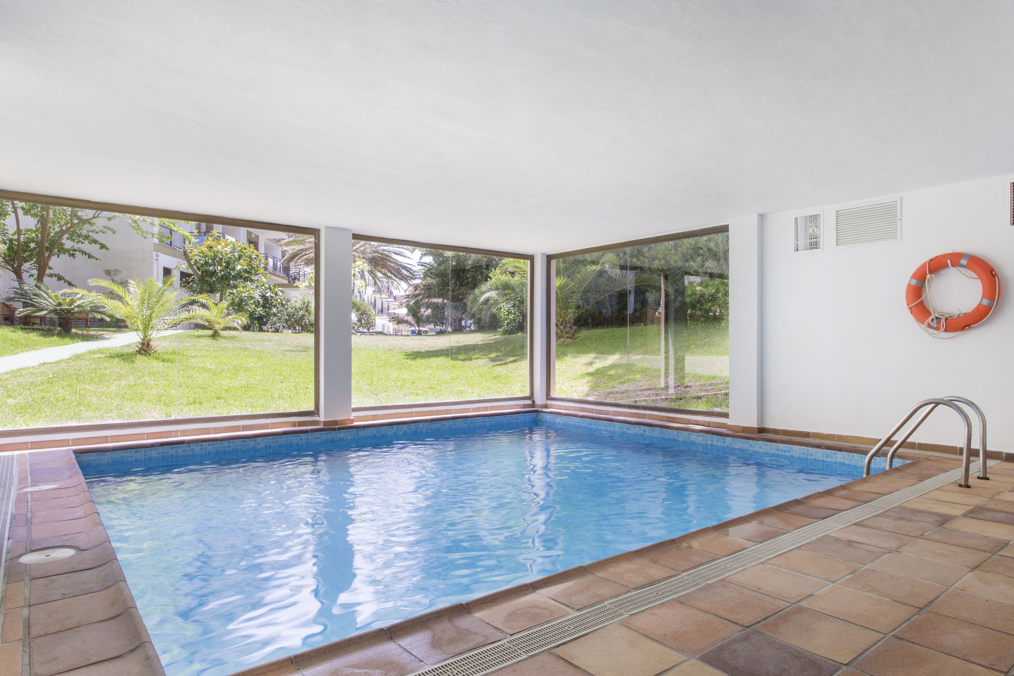 Una piscina techada, una piscina al aire libre, sombrillas