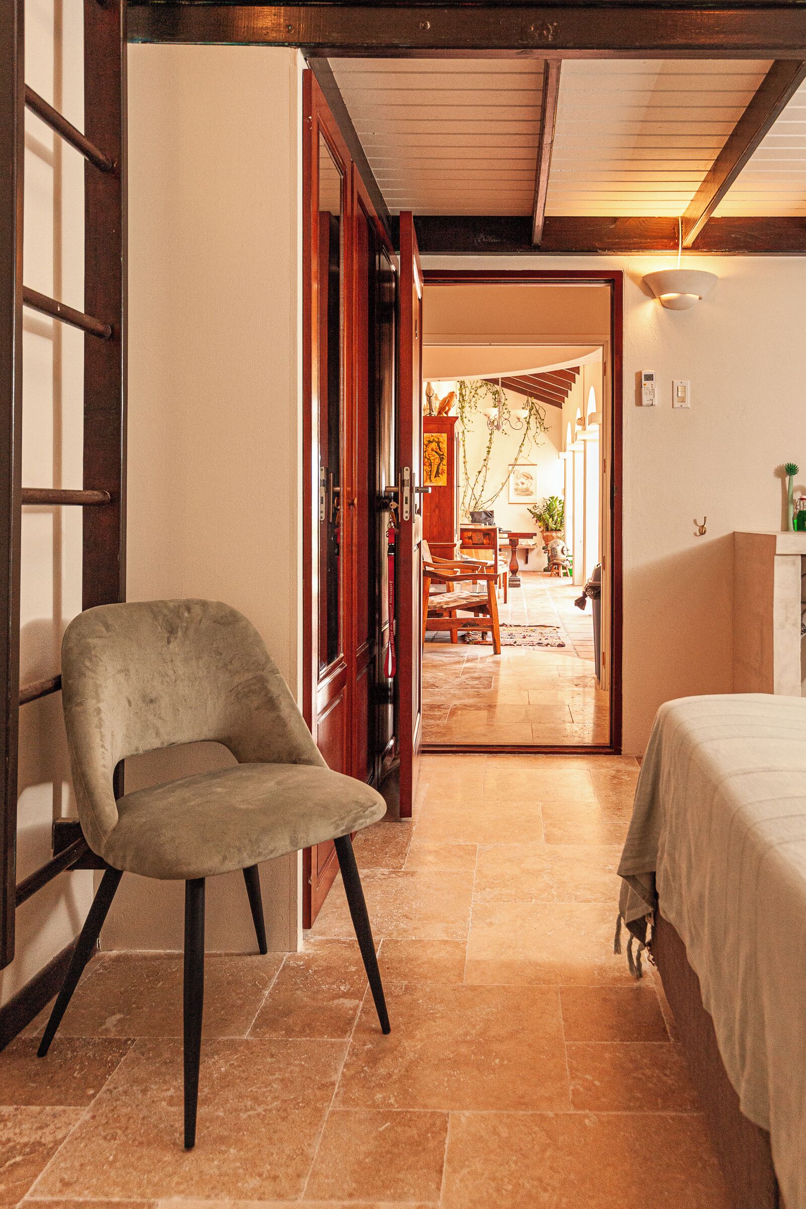 A room with a bed, a chair, and a wooden door leading to a dining area.