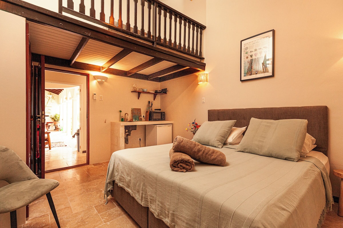 A bedroom with a bed, a chair, a desk, and a staircase.