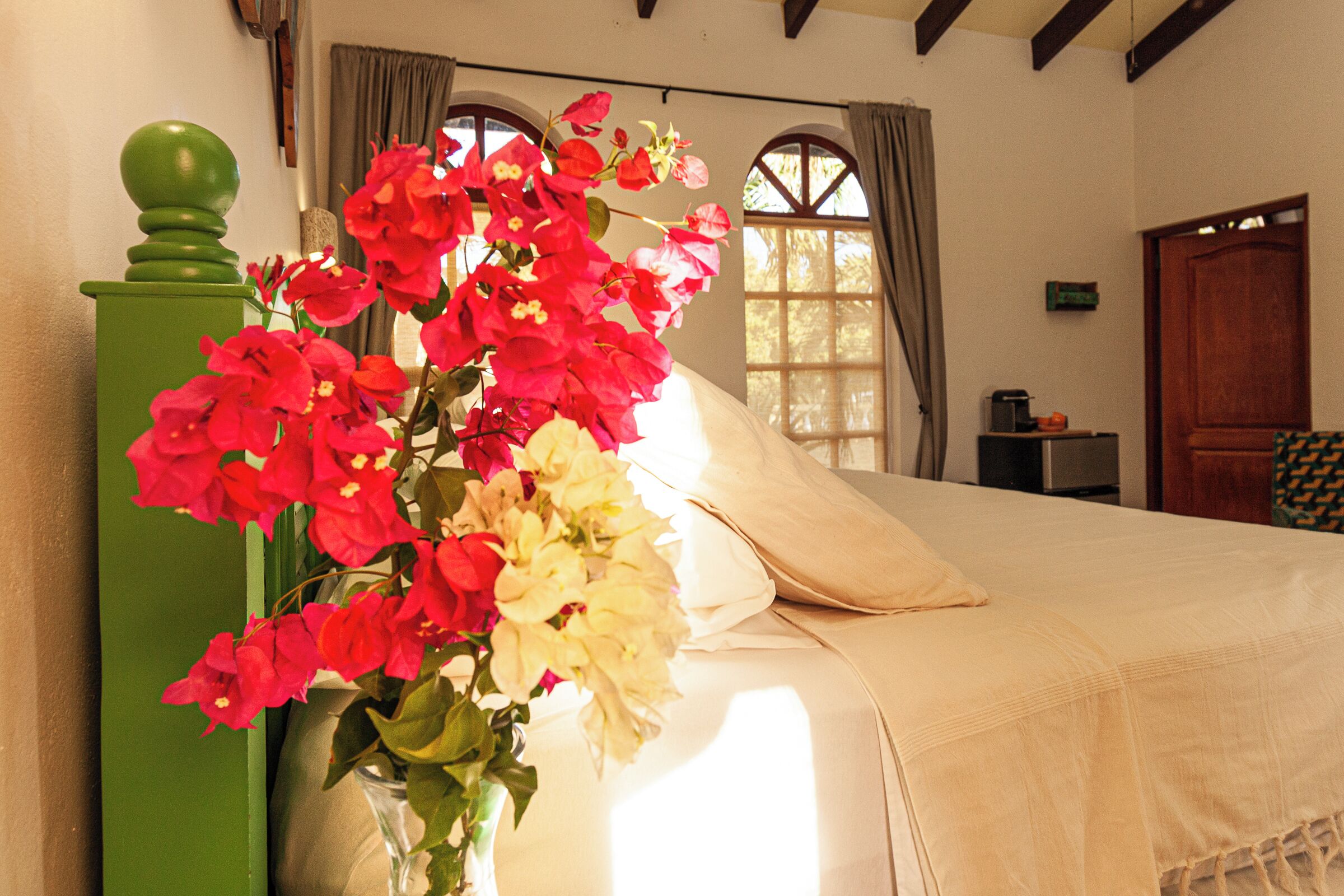 Ein Schlafzimmer mit einem Bett, einem grünen Blumenvasen und einem Fenster mit Vorhängen.