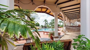 An outdoor pool area with a covered seating area, palm trees, and a view of the pool. - Goood Resort (Kralendijk)