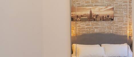 A hotel room with a bed, a cityscape artwork on the wall, and a brick-patterned backdrop.