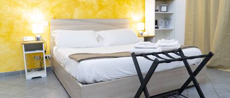 Un lit bien fait, avec du linge de lit blanc, une table de chevet avec une lampe et une étagère avec des articles de toilette.