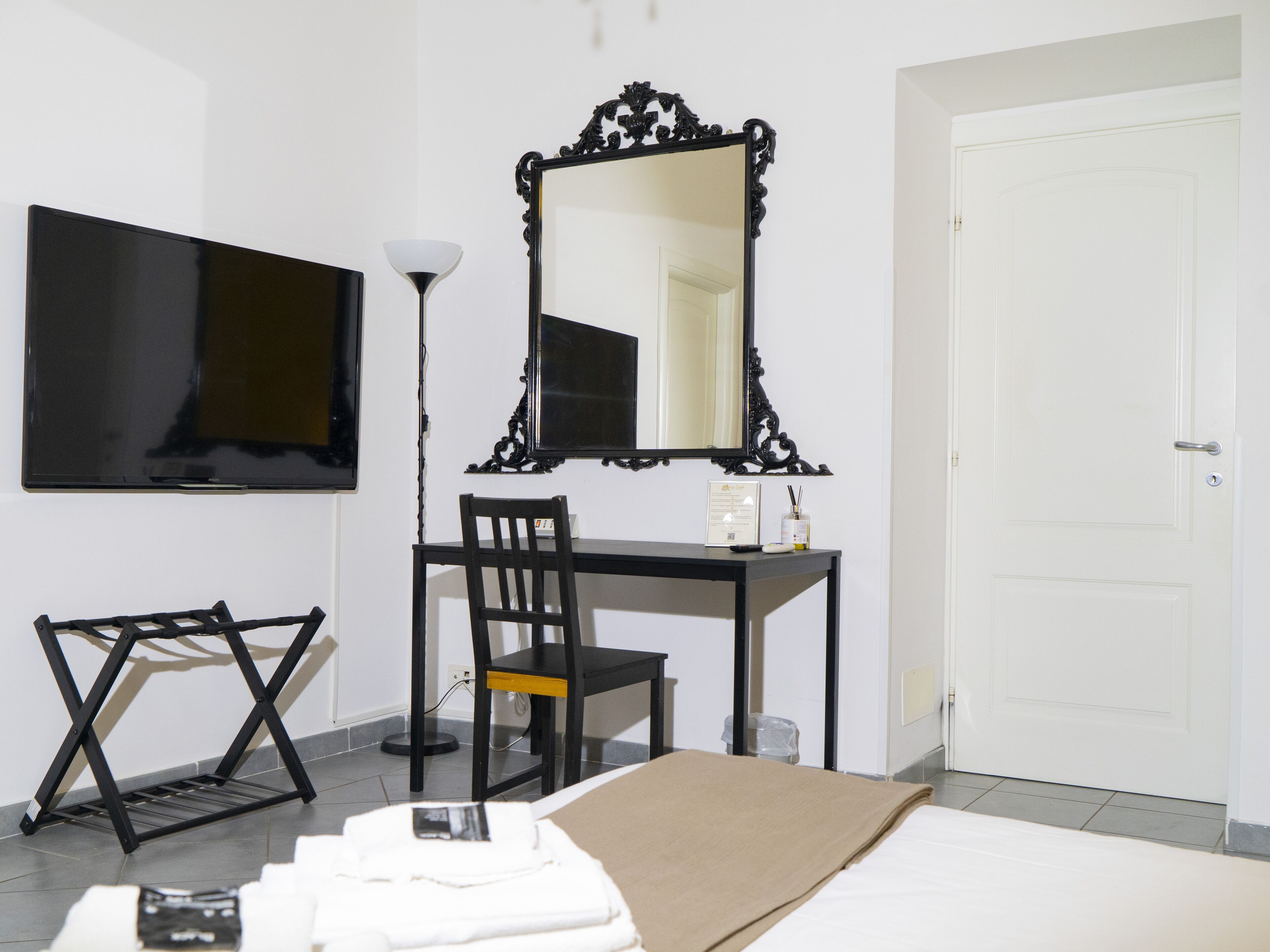 A hotel room with a bed, a desk, a chair, a TV, and a mirror.