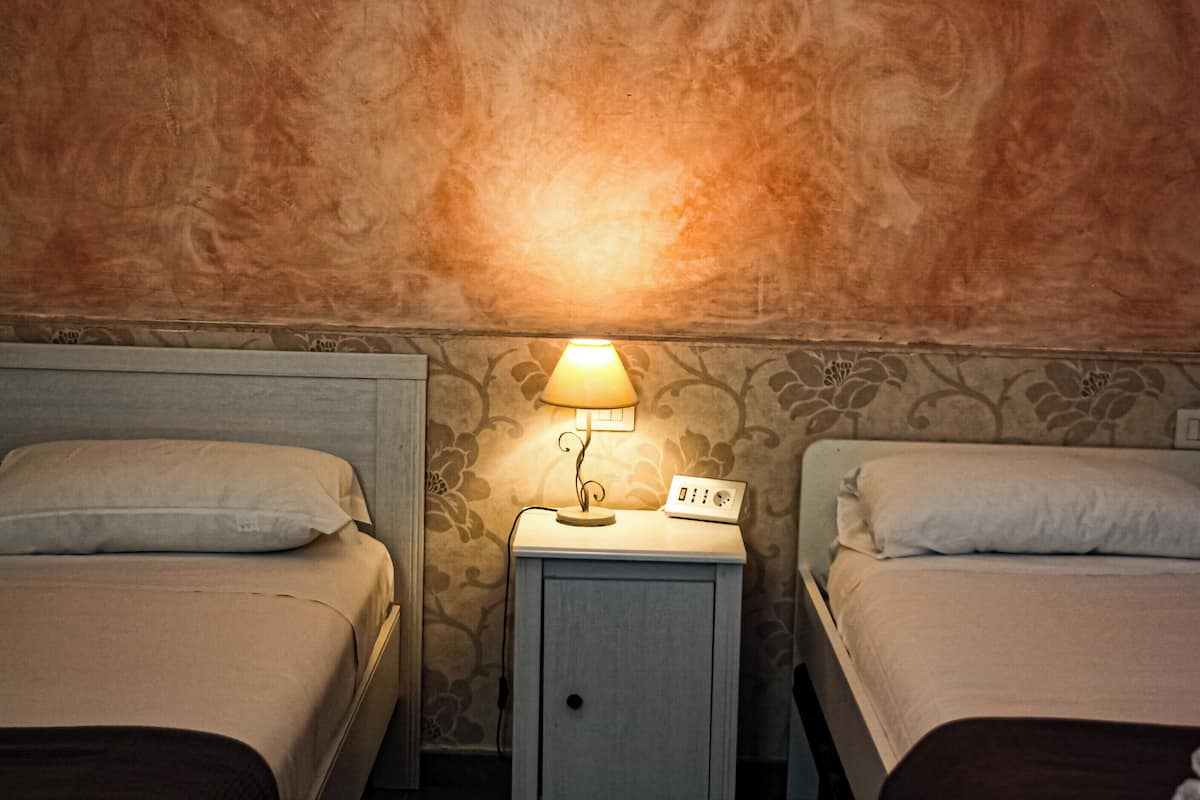 Twin beds with headboards, a bedside table with a lamp, and a wall with a floral pattern.