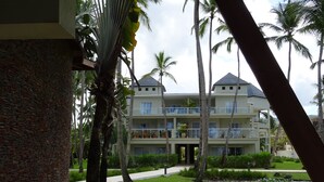 Un hôtel à plusieurs étages, doté de balcons, entouré de palmiers et d’une pelouse bien entretenue.