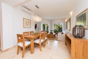 A modern living room with a wooden dining table, white sofas, and a large window with a view of palm trees. - Cosón Bay (Las Terrenas)