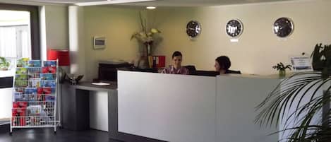 Ett väntrum med en receptionsdisk, ett tidningsställ och tre klockor på väggen.