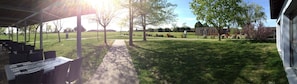 An outdoor patio area with tables and chairs, a covered seating area, and a grassy lawn with trees. - CIST Domaine d'Ariane (Mondonville)