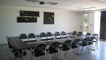Une salle de conférence avec une longue table et des chaises, un projecteur au plafond et deux compositions florales accrochées au mur.